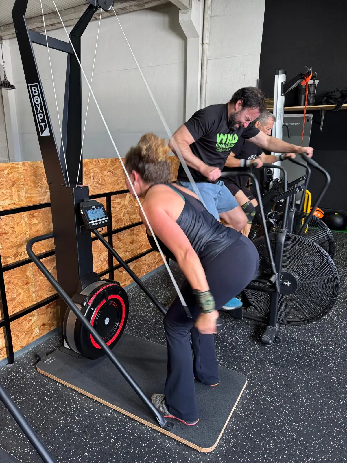 Três atletas em esforço no ski-erg e nas air bikes